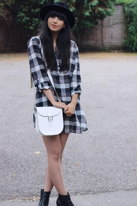 Kockované košeľové šaty v kombinácii s bielou taškou cez rameno, čiernymi čižmami a klobúkom